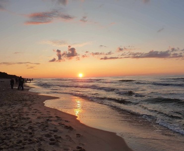 Zach&oacute;d słońca nad plażą i morzem, z delikatnymi odbiciami światła na wodzie i spokojną kompozycją.