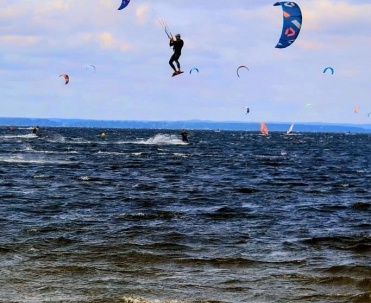 Kitesurferzy na wodzie podczas zachodu słońca &ndash; dynamiczny kadr sportowy z bardzo efektownym niebem.